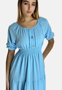 Jasnoniebieska sukienka z krótkim rękawem, marszczonym w talii, z okrągłym dekoltem i trzema ozdobnymi guzikami z przodu; miękka, teksturowana tkanina.