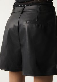 Shorts en cuir noir à texture lisse, avec une poche arrière, une coupe droite et des détails de couture subtils.