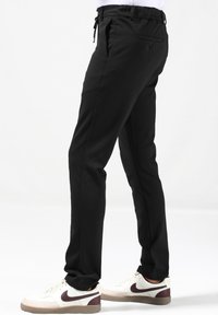 Zwarte broek met een trekkoord in de taille, zijzakken en een achterzak; gecombineerd met witte sneakers met bordeauxrode accenten.