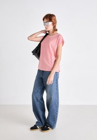 Rød og hvit stripete kortermet topp, løse blå jeans, svart sneakers med gummisåler, og en svart skulderveske. Sølvbriller gir kontrast.