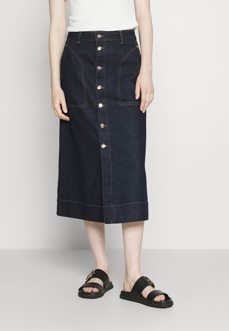 Denim midi kjol, mörkblå med synliga sömmar, knäppning fram, två stora framfickor, kombinerad med svarta sandaler.