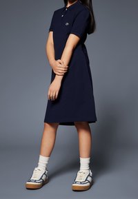 Marinblå pikétröja i bomull med korta ärmar, med br�östficka och liten logga. Kombineras med vita strumpor och mönstrade sneakers.