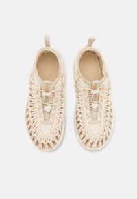Beżowe sneakersy z plecioną cholewką, teksturowaną podeszwą i regulowanymi sznurówkami. Posiadają uchwyt na pięcie ułatwiający zakładanie.