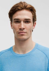 Sininen urheilupaita jossa teksturoitu kuvio, pyöreä pääntie ja lyhyet hihat. Sileä kangas, istuva malli ja kontrastisaumat.