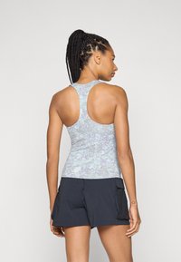 Top de alças racerback ajustado em padrão tie-dye azul claro e roxo, combinado com calções escuros com bolsos laterais e detalhes em malha.