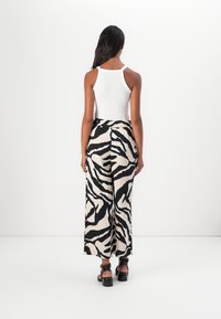 Débardeur blanc, pantalon large avec un imprime zèbre noir et crème, sandales noires plates, cheveux tombant sur le dos, texture lisse.
