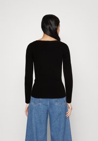 Schwarzes, geripptes Langarmoberteil mit weiter Ausschnittkante, tailliert, kombiniert mit hellblauen, weiten Jeans und einer glatten Stoffstruktur.