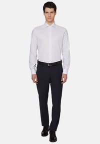 Bela dolgimi rokavi srajca s slim fit krojem, gumbi spredaj in pointed ovratnikom, v kombinaciji s temnimi hlačami in črnimi čevlji.