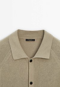 Cardigan beige en tricot avec un col côtelé et deux boutons noirs sur le devant, montrant la partie supérieure de la poitrine et des épaules.