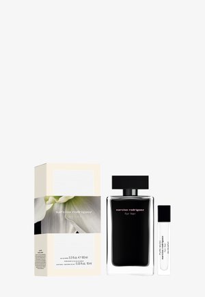 Flacon de parfum en verre noir avec un capuchon carré, accompagné d'un vaporisateur de voyage transparent et d'un emballage présentant un motif floral aux couleurs douces.