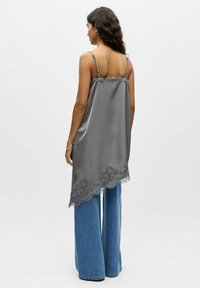 Camisole gris en satin avec bretelles ajustables et bordure en dentelle florale, associée à un jean en denim à jambes larges. Texture lisse et ourlet asymétrique.