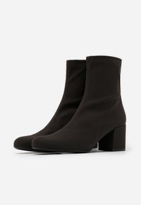 Svarta ankelboots med en slank, stretchig textilöverdel, spetsig tå och klack med blockdesign. Slät yta, minimalistisk design, ingen synlig hårdvara.