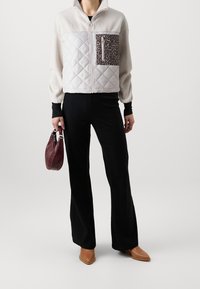 Beige tikattu takki, jonka yläosa on teksturoitu, leopardikuvioinen tasku, mustat ribbineulotut housut ja ruskeat kärkikärjelliset kengät. Ruskea laukku.