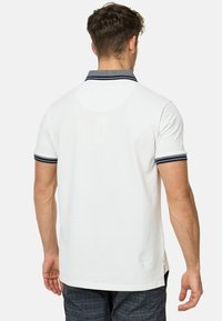Hvid polo skjorte med en marineblå krave og manchetter, korte ærmer og slidser i siden ved kanten for nem bevægelse. Tekstureret stof.