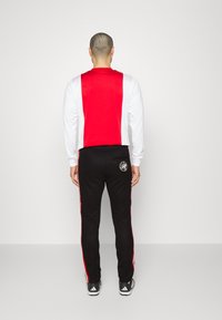 Track suit featuring a red and white long-sleeve top and black pants with red side stripes. Textured fabric with side logo detail.