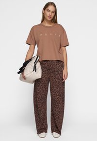 T-shirt cropped a maniche corte marrone con stampa "TODAYS"; abbinato a pantaloni a gamba larga marroni con una stampa leopardata scura e una borsa a spalla crema.
