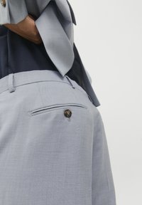 Lichtblauwe op maat gemaakte broek met een gladde textuur, voorzien van een achterzak afgesloten met een donkere knop en een strakke tailleband.