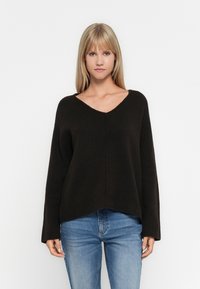 Brun, strikket genser med V-hals, løs passform og ribbestrikkede mansjetter. Sammen med blå jeans har den en myk tekstur og enkelt design.