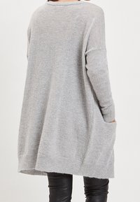 Šedý oversized svetr s uvolněným střihem, dlouhými rukávy a postranními kapsami, vyrobený z měkké pleteniny.