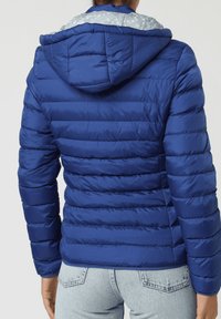 Chaqueta acolchada azul con capucha, que presenta un diseño acolchado horizontal, tejido brillante y un forro interior claro con patrón. Esquema de colores azul y gris.