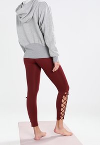 Grey hoodie with a spacious fit paired with burgundy leggings featuring a side cut-out design and lacing detail on the lower legs.
