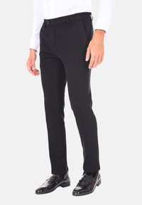 Pantaloni neri su misura con vestibilità slim, tessuto liscio e chiusura a un bottone, abbinati a mocassini neri lucidi.