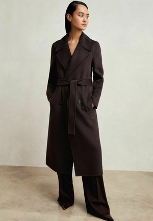 Ruskea villa-trench-takki, jossa on leveä kaulus, kaksirivinen etuosa, vyötärölle sidottu vyö ja sivutaskut. Silkkinen pinta, muotoiltu malli.