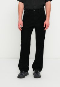 Μαύροι παντελόνια από κορδόνι βελουτέ με ίσια εφαρμογή, τσέπες μπροστά και κούμπωμα με κουμπιά. Συνδυασμένα με γκρι αθλητικά παπούτσια.