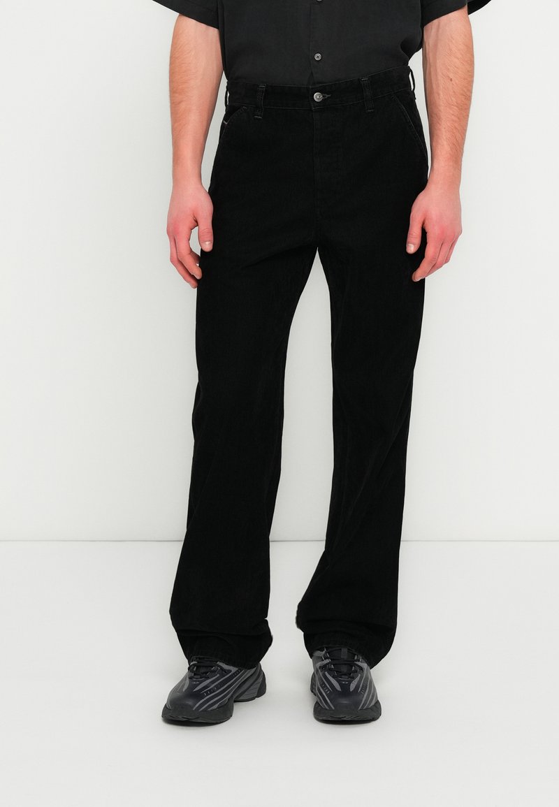 Μαύροι παντελόνια από κορδόνι βελουτέ με ίσια εφαρμογή, τσέπες μπροστά και κούμπωμα με κουμπιά. Συνδυασμένα με γκρι αθλητικά παπούτσια.