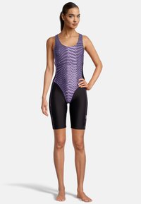 Maillot de bain violet et noir avec un motif en écailles, doté d'une coupe ajustée et de shorts, fabriqué en matériau extensible et résistant à l'eau.