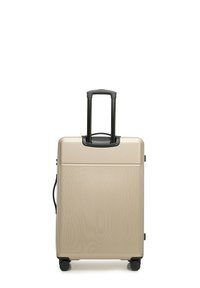 Harde koffer in metallic goud, met verticale ribbels, een uitschuifbare zwarte handgreep en vier zwarte wielen voor mobiliteit.