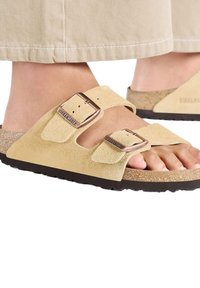Sandali in suede beige con due cinturini regolabili e fibbie metalliche, dotati di una soletta in sughero e una suola nera testurizzata.