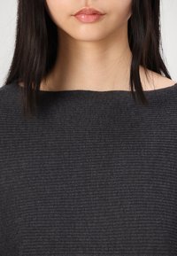 Ciemnoszary dzianinowy sweter o szerokim dekolcie i prążkowanej fakturze. Materiał wydaje się miękki i dopasowany wokół szyi oraz ramion.