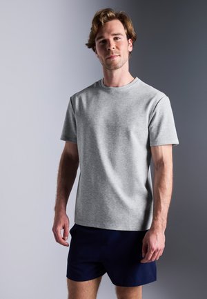 T-shirt in cotone grigio con colletto rotondo e maniche corte, abbinata a pantaloni corti blu navy. Il tessuto ha una consistenza morbida e una leggera lucentezza.