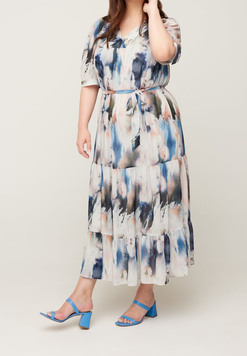 Femme portant une robe tie-dye mi-longue à manches courtes avec ceinture à la taille, associée à des sandales à talons blocs bleu clair.
