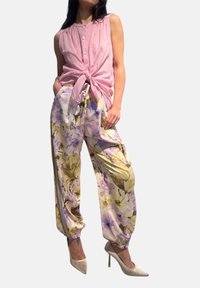 Canottiera rosa senza maniche con dettagli a bottoni, abbinata a pantaloni stampati floreali in delicate tonalità di viola e giallo, completati da polsini elasticizzati.