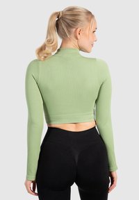 Ljusgrön, randig långärmad cropped topp med hög hals, i kombination med höga svarta leggings som visar en smal passform och slät textur.