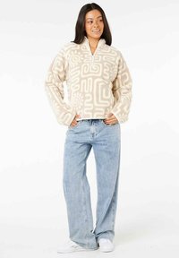 Fleece half-zip trøje i creme med abstrakte beige mønstre. Sæt den sammen med lyseblå vide jeans og hvide sneakers.