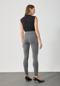Black sleeveless top paired with fitted gray leggings. The leggings feature a smooth texture and a high waist, complemented by black heels.