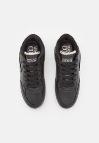 Svarta lädersneakers med vadderad krage, snören och vit gummisula. Har logotyp på innersulan och en kontrasterande beige detalj.