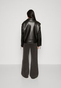 Black leather jacket with a wide, structured collar and long sleeves, paired with gray wide-leg pants. Smooth texture, minimal detailing.