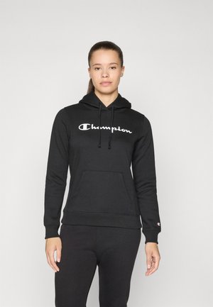 Svart bomullshoodie med frontlomme og snor. Den har en hvit "Champion"-logo på brystet og matchende svarte bukser.