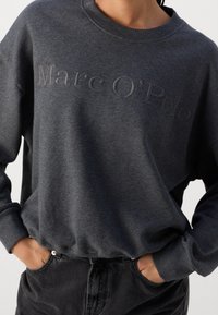 Felpa grigia scura con scollo a girocollo, caratterizzata da un logo "Marc O'Polo" in rilievo sul petto e polsini a coste. Tessuto morbido.