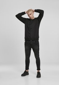 Svart genser med lange ermer og rund hals, kombinert med mørk denim jeans og svarte joggesko. Uformell, tettsittende design med minimalistiske detaljer.