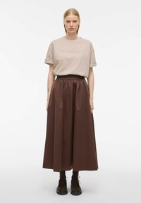 Beżowy t-shirt z wytłoczonym napisem "ROUGE EDIT", w zestawieniu z długą, brązową, plisowaną spódnicą. Modelka nosi ciemne buty i skarpetki. Prosty design.