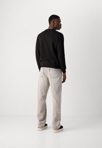 Felpa nera con colletto rotondo, abbinata a jeans grigi chiari con due tasche posteriori. L'outfit è completato da sneakers nere.