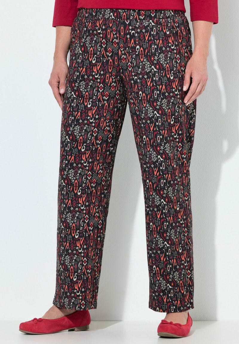 Černé kalhoty s barevným geometrickým vzorem v červené, bílé a šedé; elastický pas; spárované s červenými plochými botami.