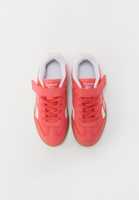Reebok tenisice s svijetlo koraljnom gornjom površinom, bijelim detaljima, vezicama i čičak trakama, te gumiranim potplatom.