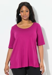 T-shirt magenta a maniche corte in tessuto morbido con scollatura ampia e spacchi laterali, abbinato a pantaloni neri. Nessun motivo o dettagli in metallo.