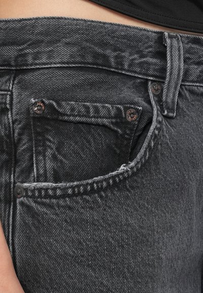 Μαύρα τζιν από τζιν ύφασμα με εφαρμοστή γραμμή, μπροστινή τσέπη με εμφανές κουμπί και υφή φθαρμένου υφάσματος.